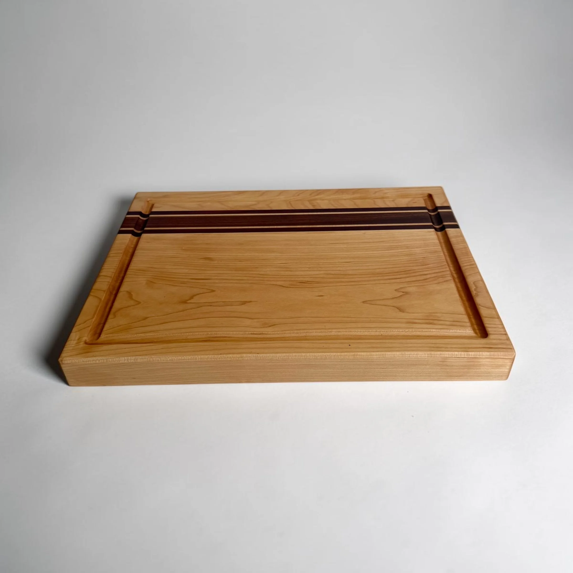 Maple cutting board with sapele and padauk accent stripes and juice groove, top-angled view