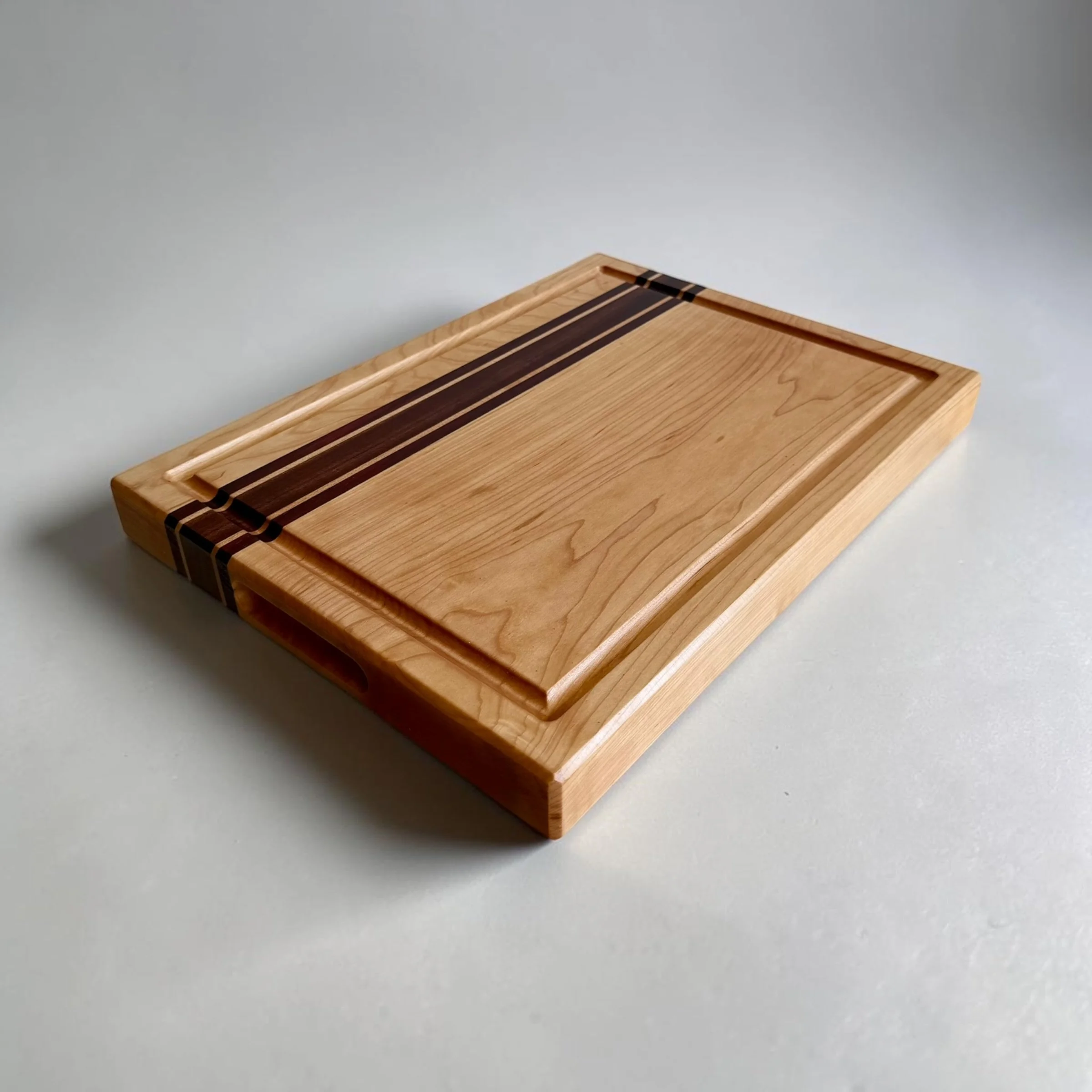 Maple cutting board with sapele and padauk accent stripes and juice groove, angled view
