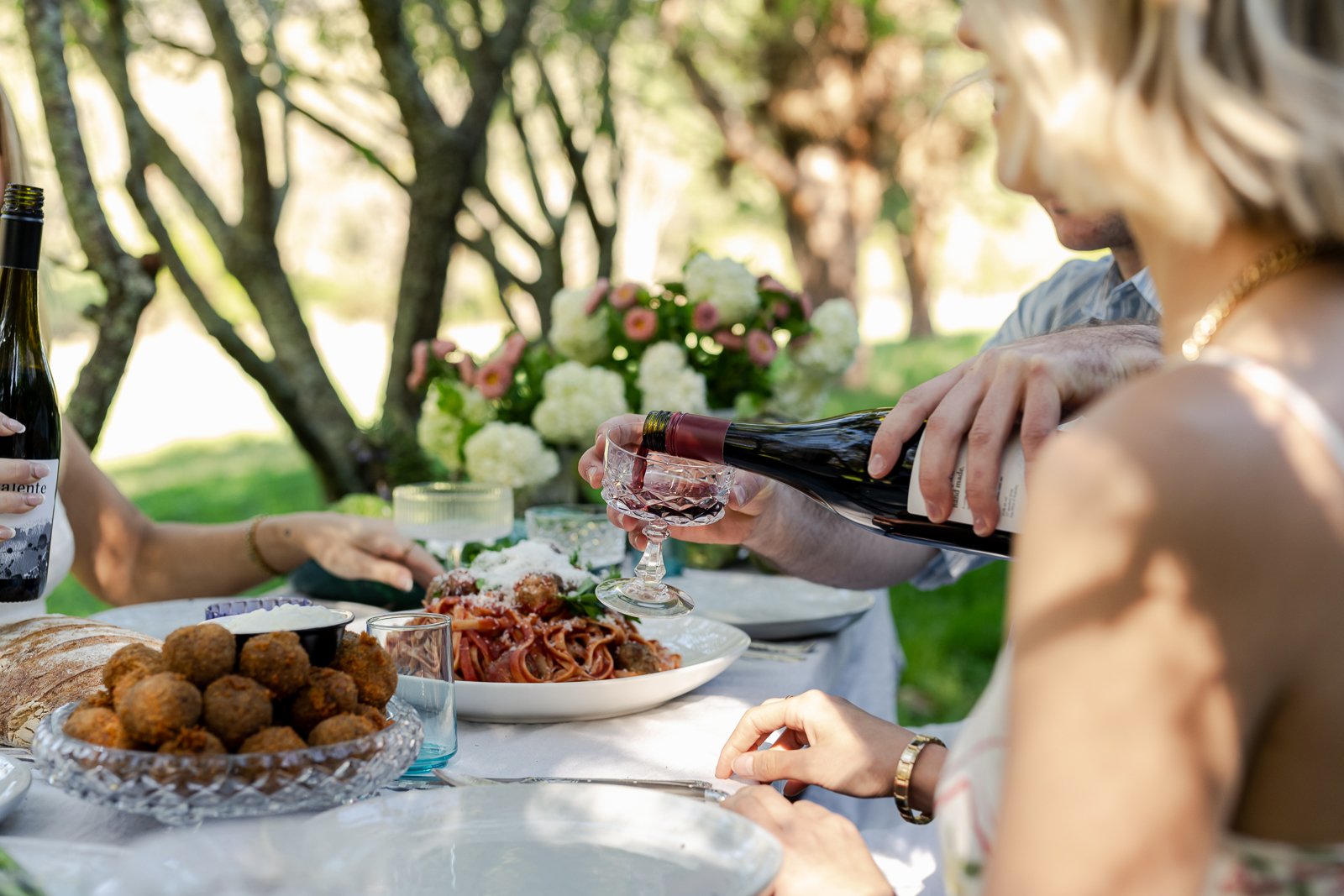 Friends sharing food, laughter and conversation around an outdoor table. Honest lifestyle photography by Georgie James Photography.