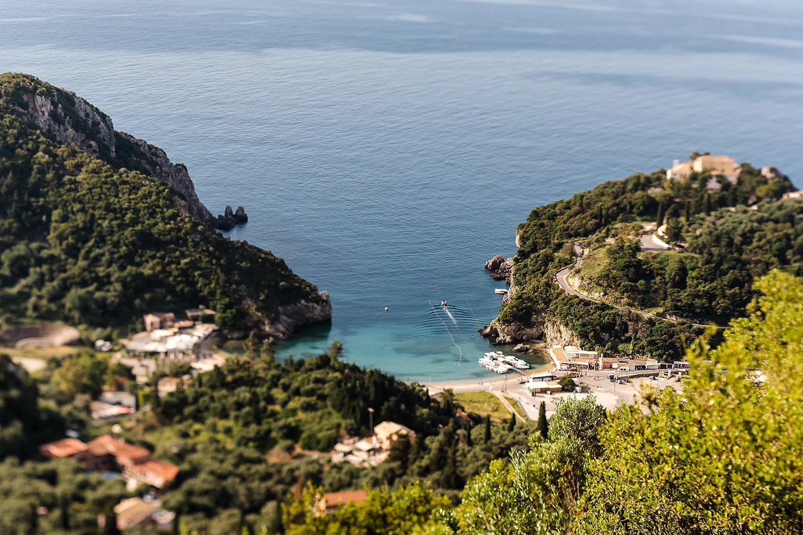 the view of paleokastritsa in corfu from the hills above - looking down to a secluded cove with a strip of beach, the village and boats and of course that bright blue water