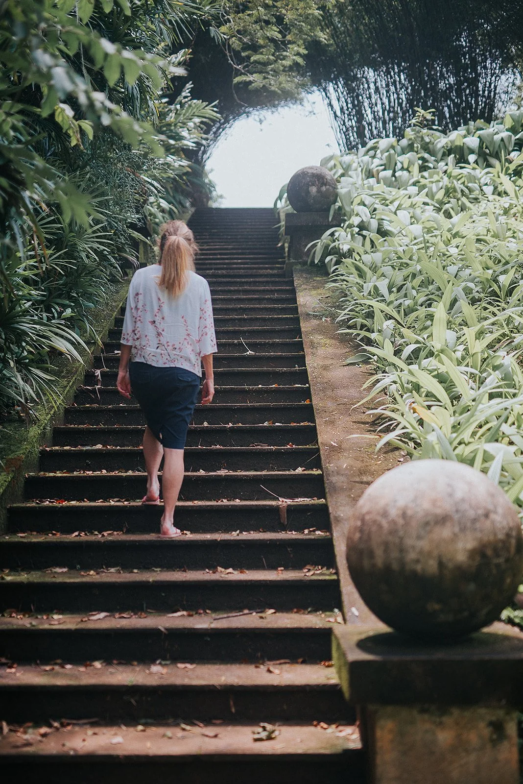 A woman climbs stone steps exploring a tropical garden.