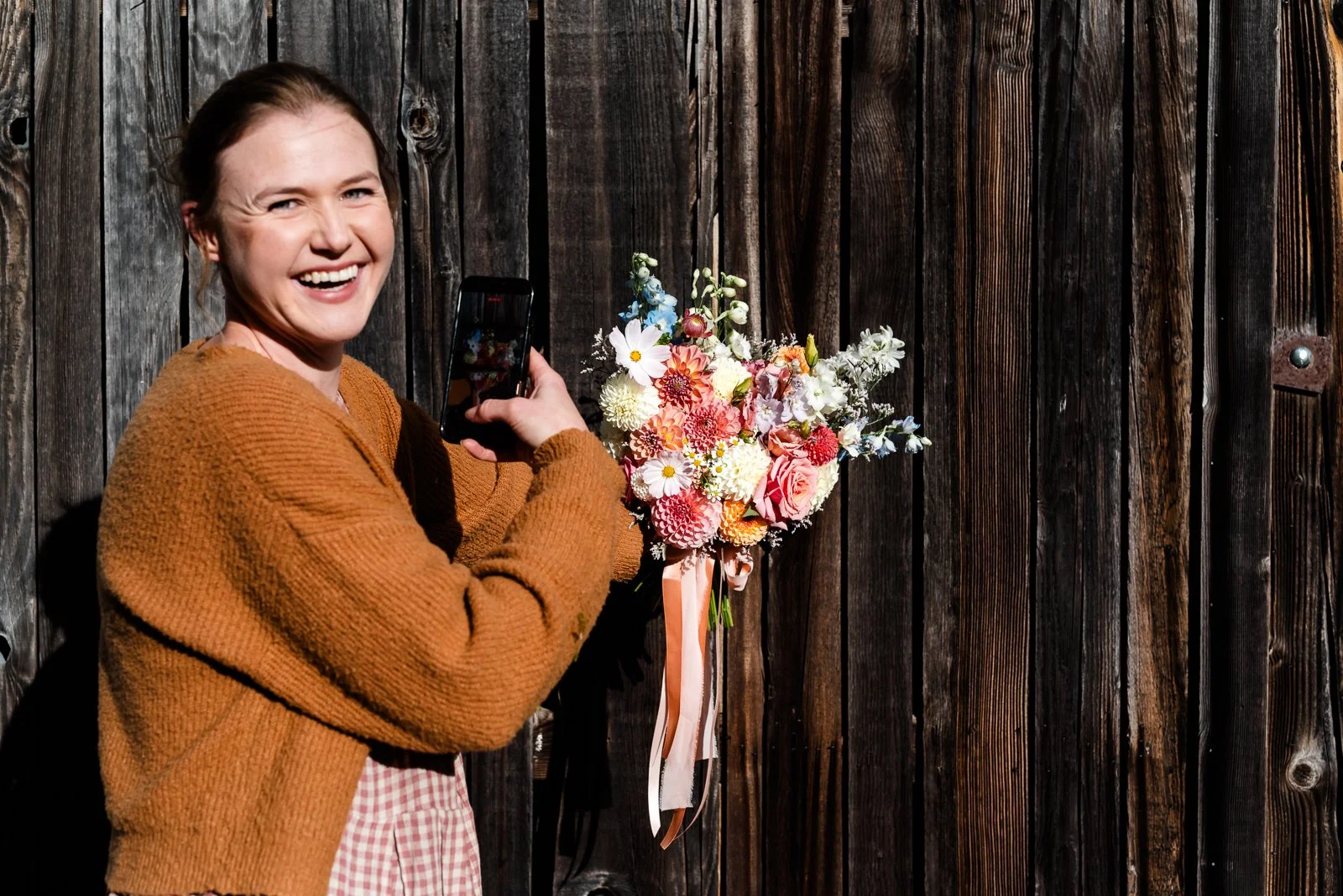 A florist smiling while photographing a freshly made bouquet with her phone. Storytelling business photography by Georgie James Photography.