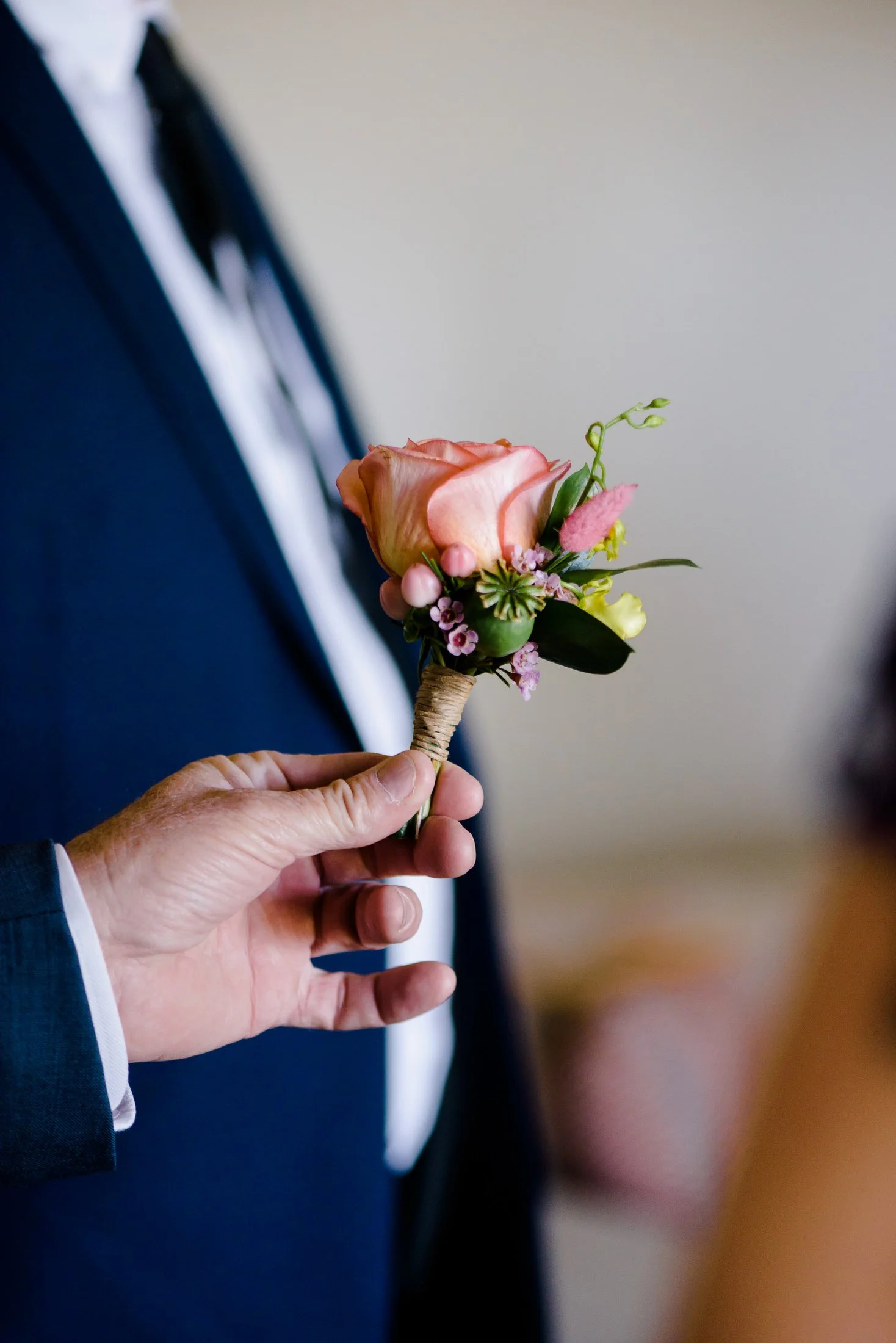 a groomsman holds the buttonhole in their hand for the groom