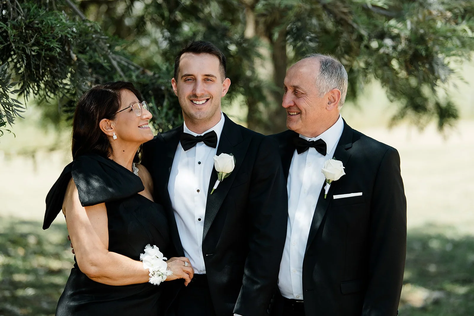 groom stands with his mother and father for a family portrait before heading to the ceremony