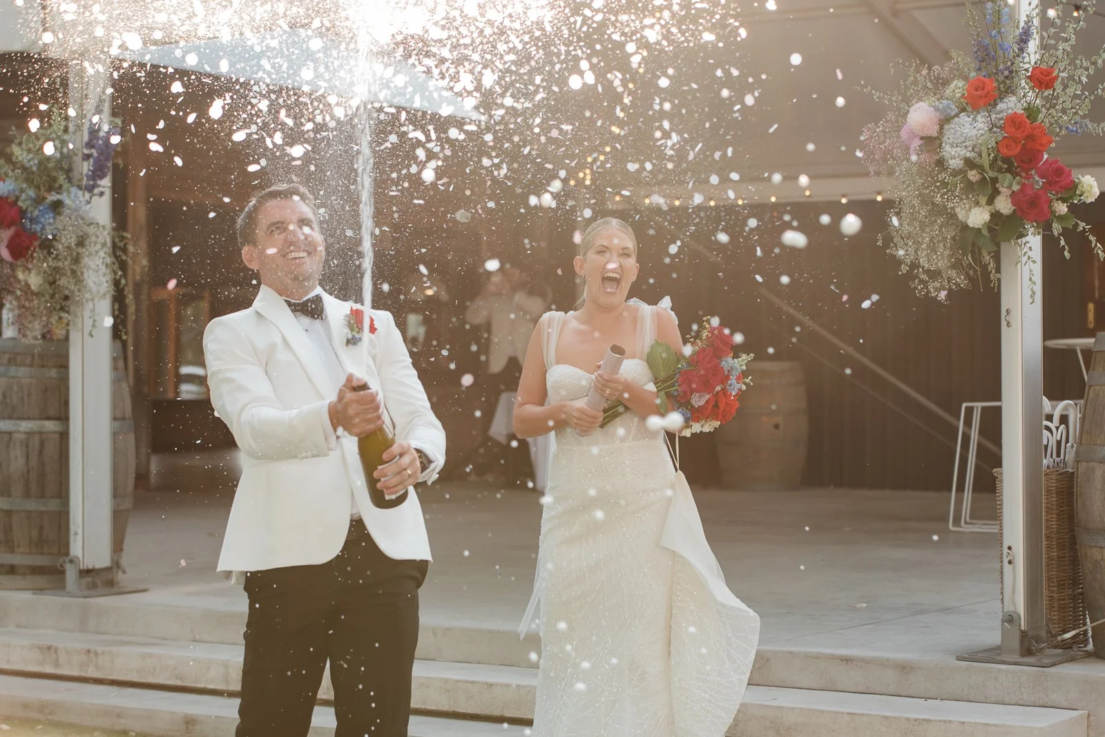 Bride and groom celebrate with a champagne spray outside their Wagga Wagga wedding reception surrounded by golden afternoon light.