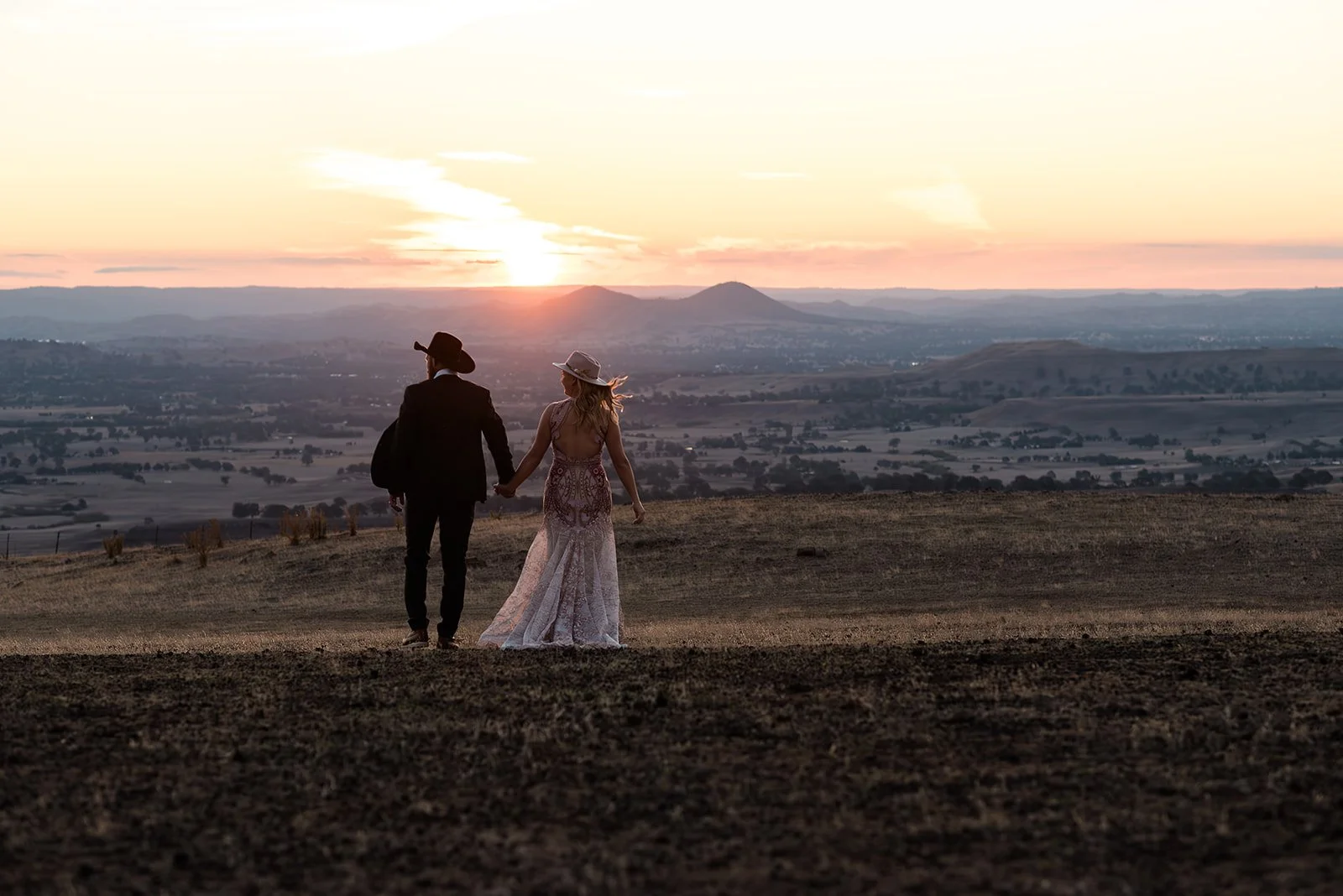couple stand on a hill looking toward the sunset