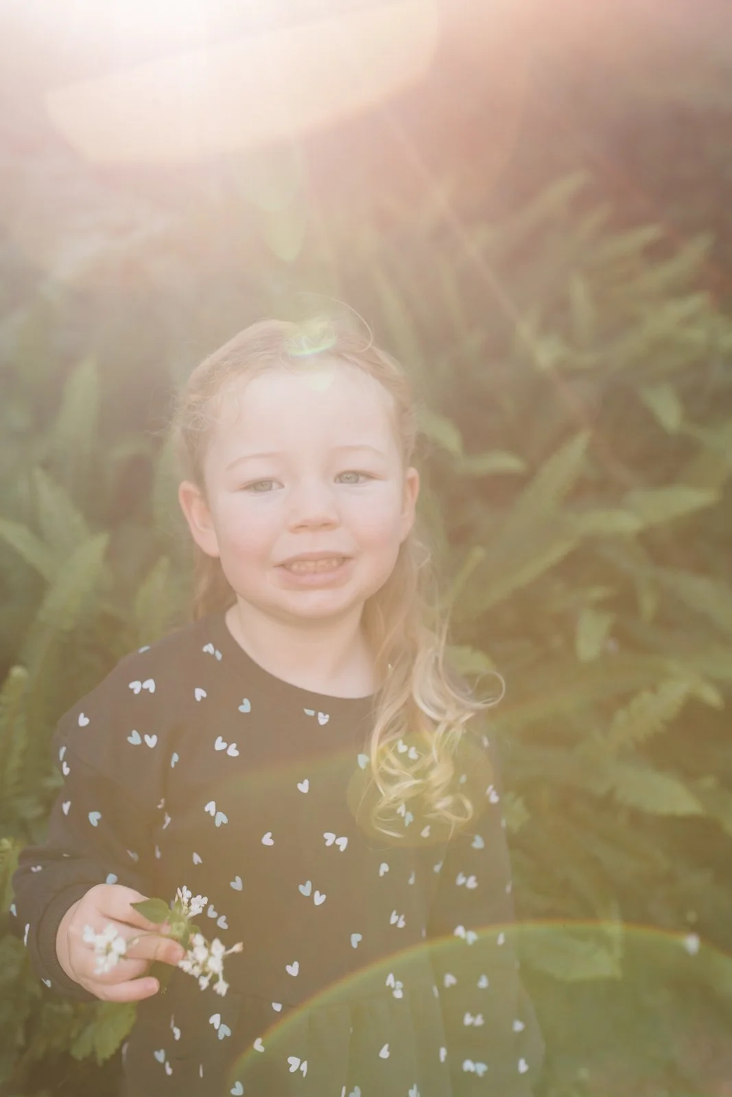 Young girl standing in soft afternoon light with flowers in her hand.