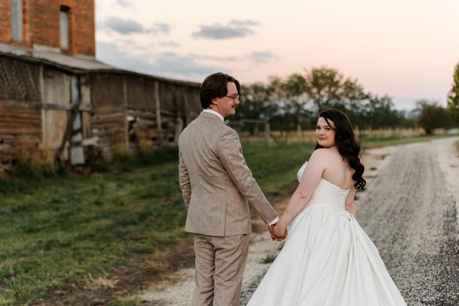 Couple holding hands on a country road at sunset after a relaxed regional Victoria wedding.