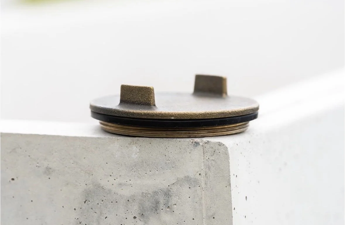 Close-up of a round metal object placed on a concrete surface, with a white background.