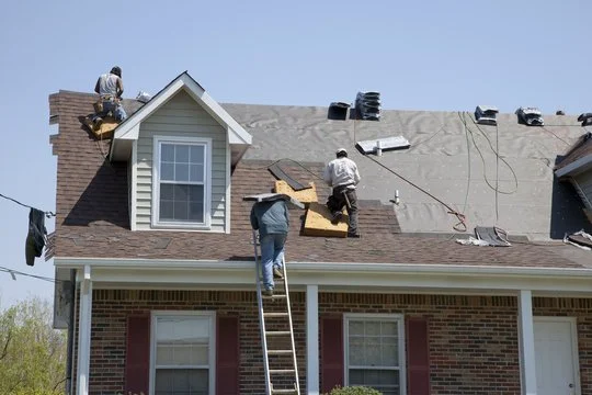 Construction workers installing roofing on a house with a brick lower level and a gray shingled upper level
