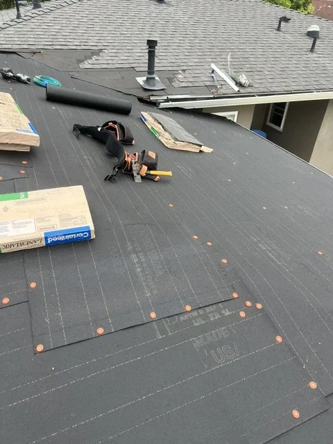 View of a roof undergoing installation or repairs, with tools, wooden boards, and roofing materials scattered across the surface.