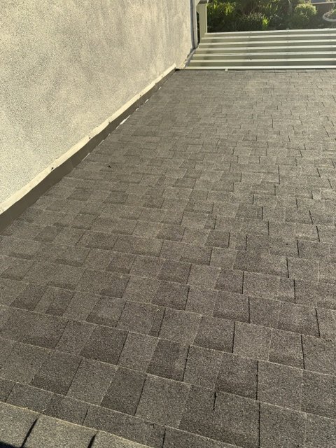 A paved outdoor patio with gray bricks, bordered by a beige edge and a white fence at the back.