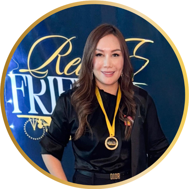 A woman with long brown hair smiling, wearing a black jacket and a gold medal around her neck, standing in front of a blue backdrop with gold lettering.
