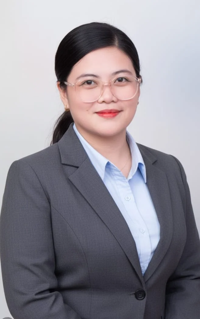 Professional woman with glasses, wearing a gray suit and light blue shirt, smiling against a plain background.