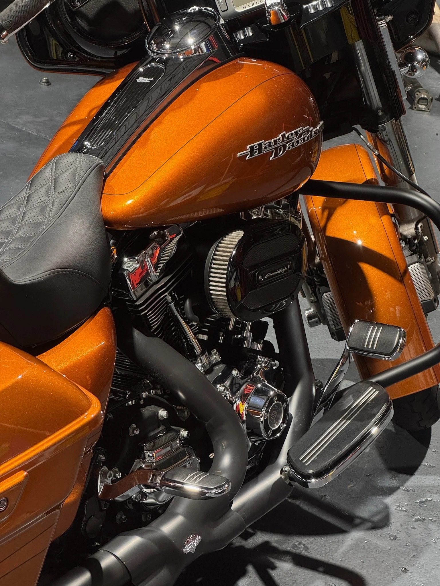 Close-up of an orange Harley Davidson motorcycle showing the fuel tank, engine, seat, and exhaust pipes.