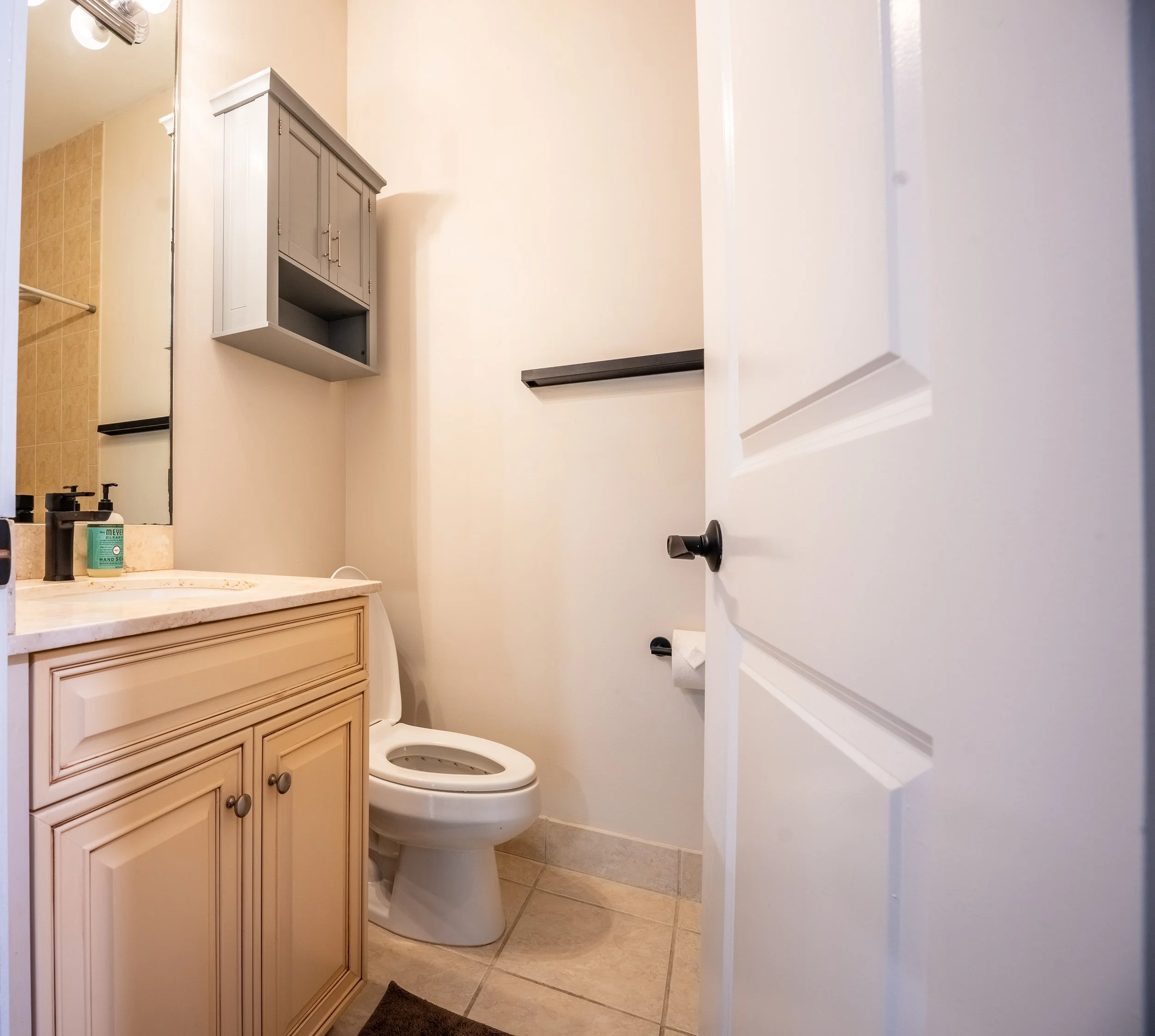 Bathroom with beige vanity cabinet, toilet, wall-mounted cabinet, towel bar, and a mirror.
