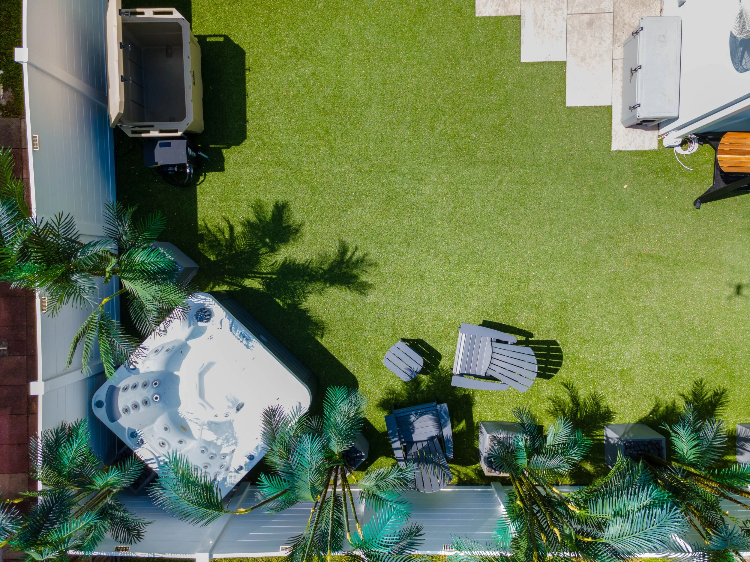 A backyard with a white hot tub, outdoor chairs, green grass, and palm trees.