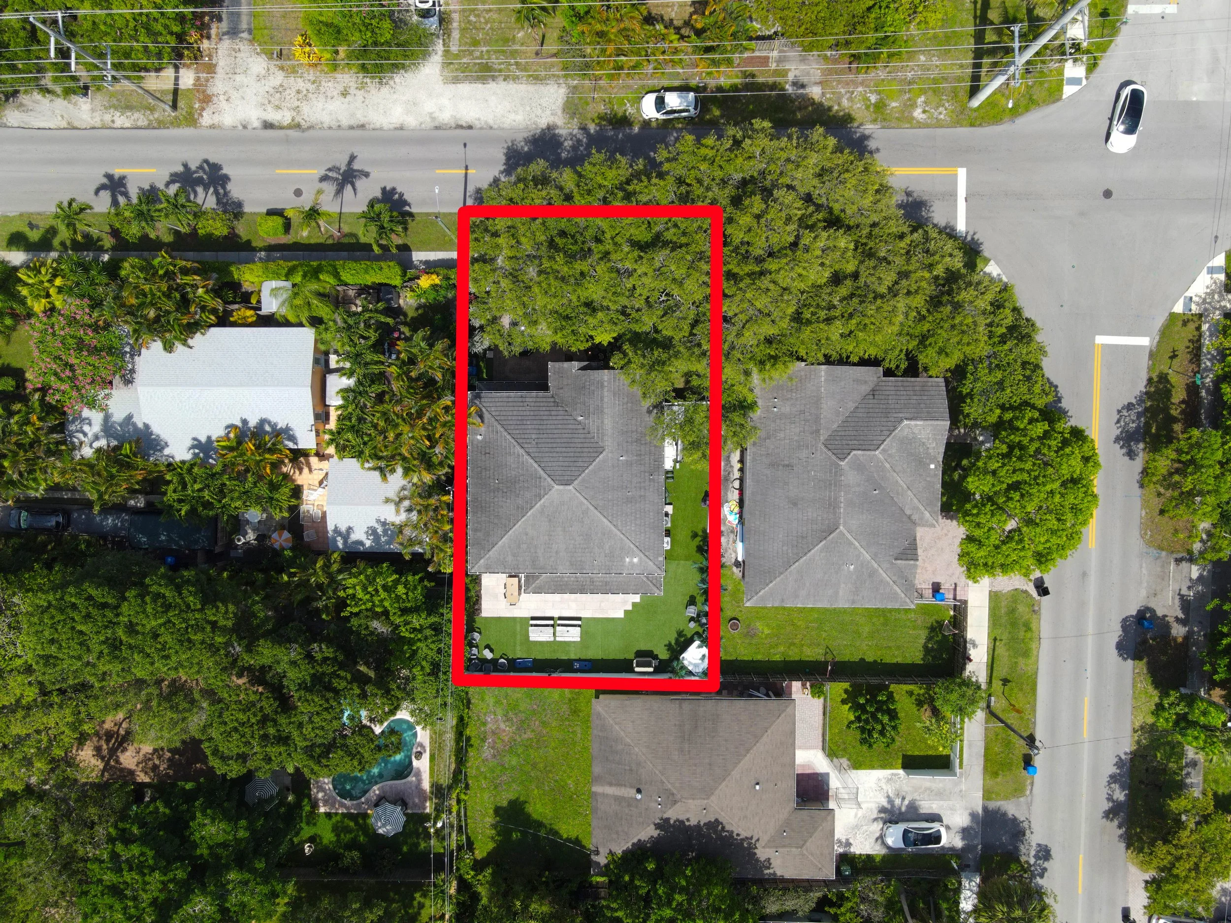 Aerial view of a residential backyard with a house, surrounded by trees, fences, and neighboring houses. The backyard is outlined with a red border.