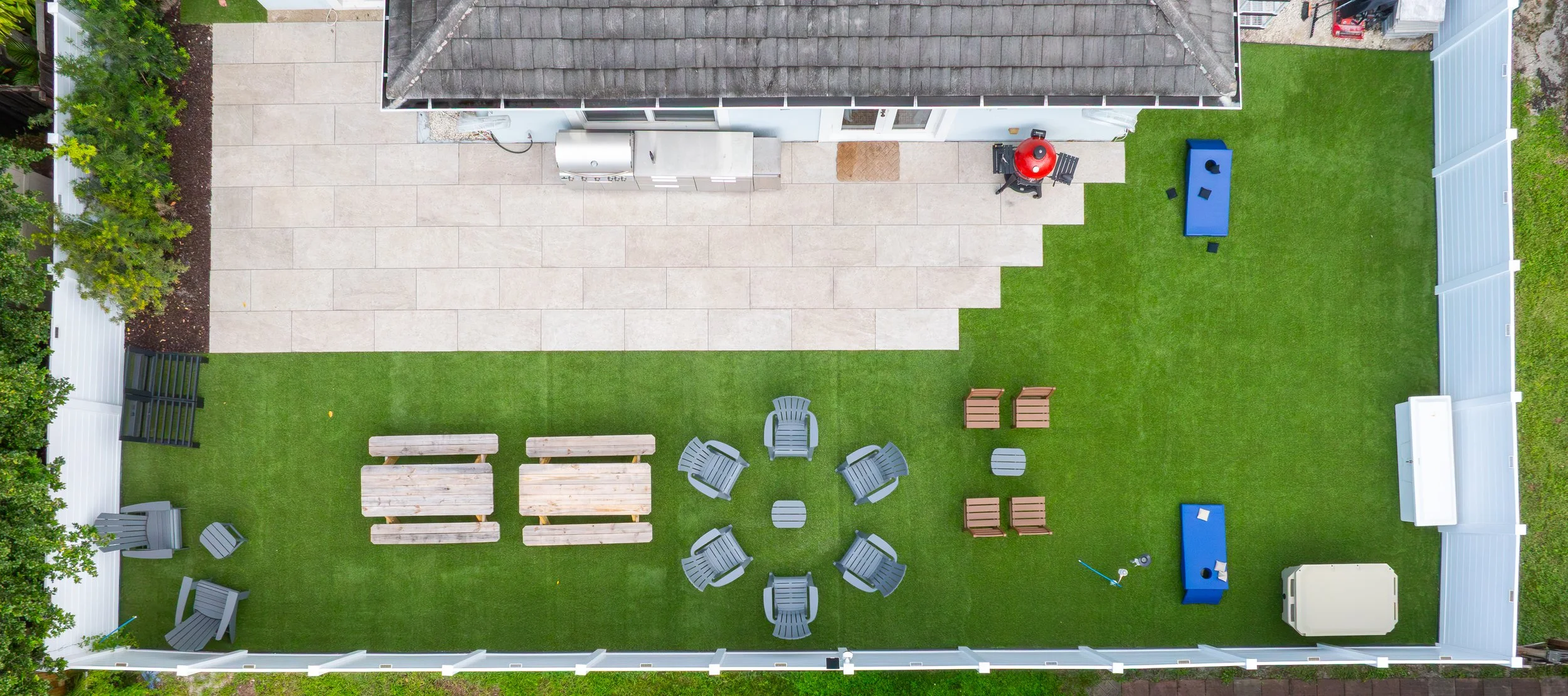 A backyard with a green lawn, outdoor furniture, a patio with a grill, and a fenced perimeter.