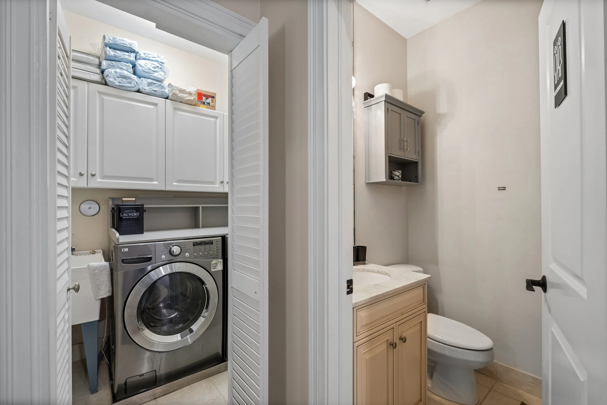 Laundry area and half bathroom with closed louvered doors, washing machine, small sink, cabinets, and a toilet.