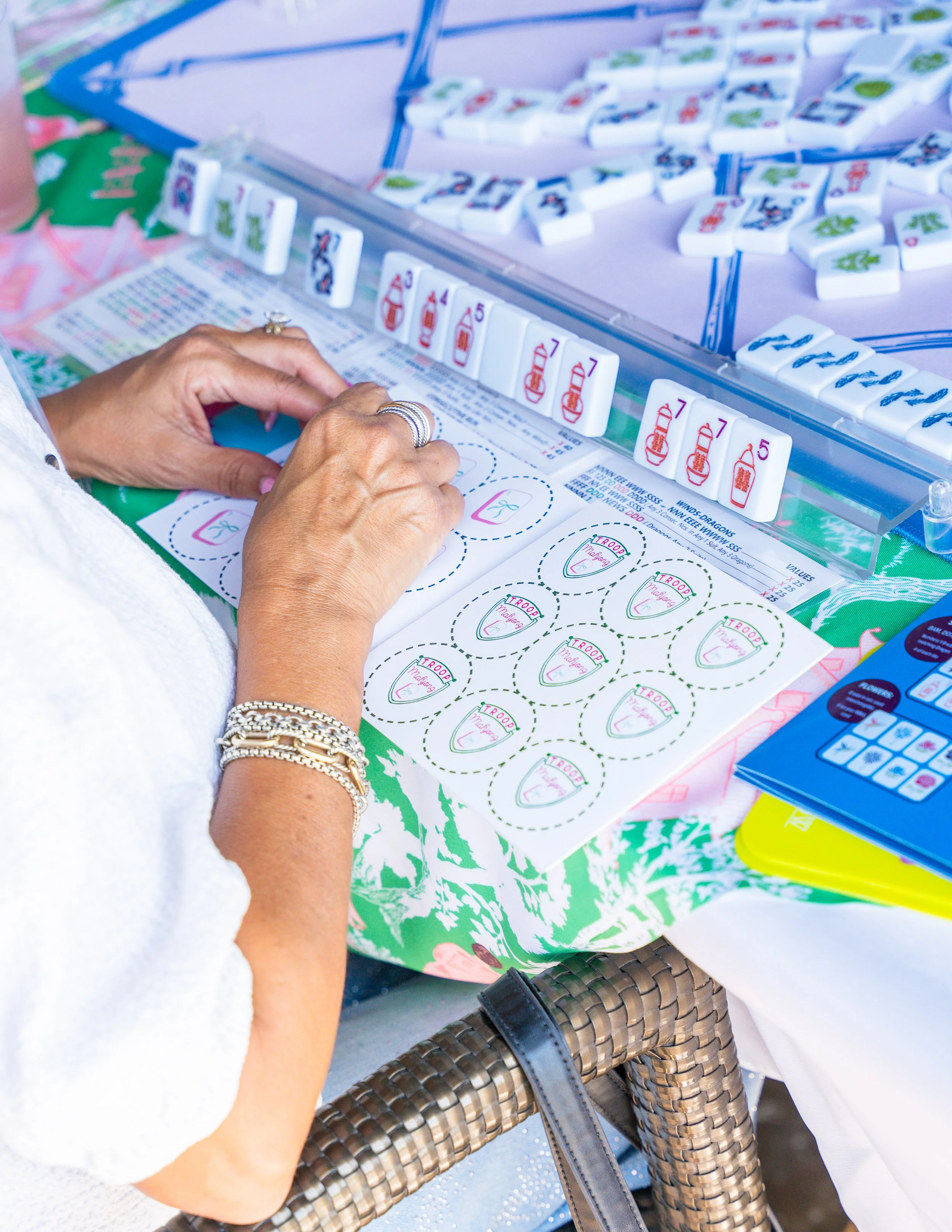 Close-up of a person's hands playing a game of Mahjong, with a Mahjong table and chips in the background.