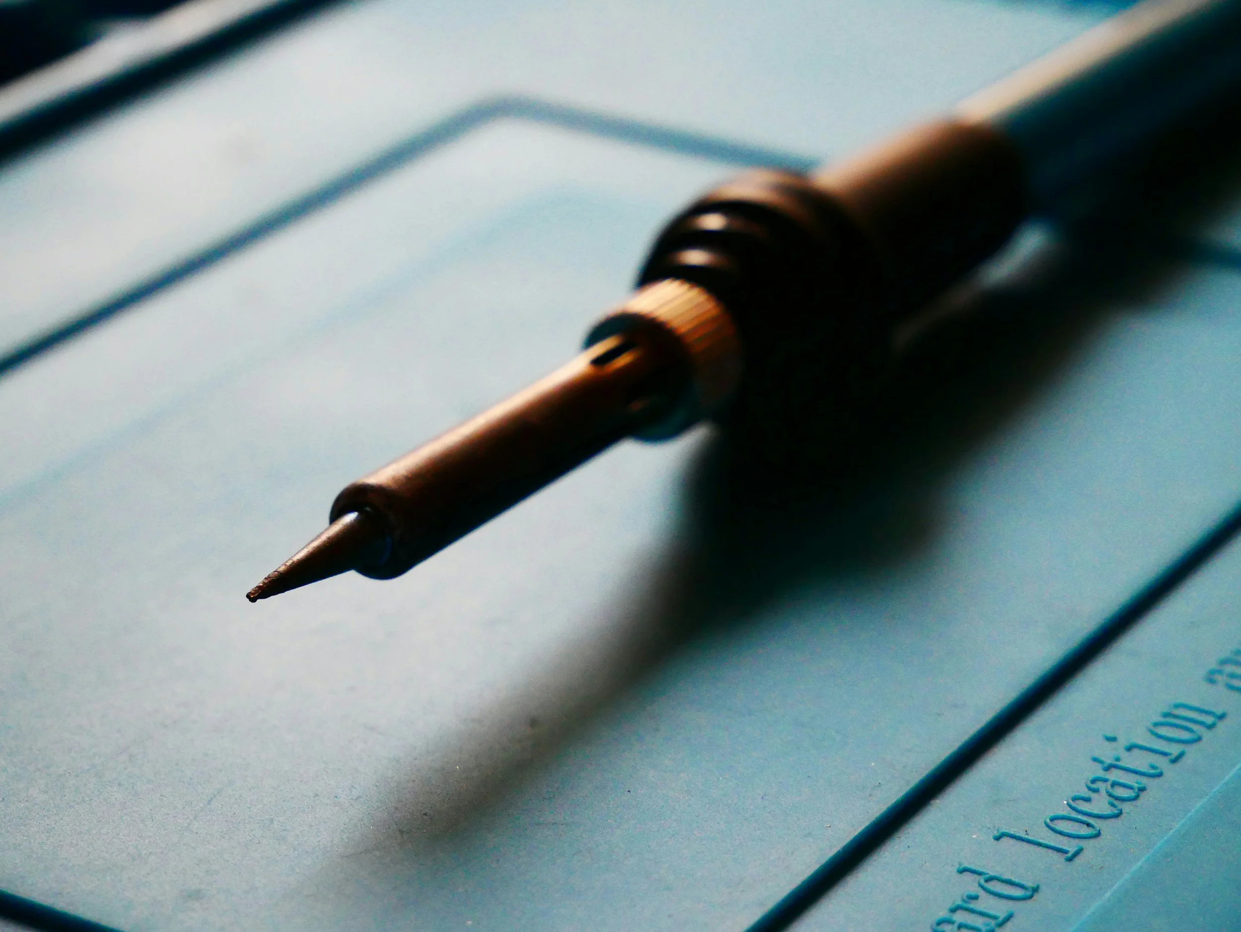 Close-up of a pyrography pen resting on a sheet of paper or notebook, with handwritten text visible.