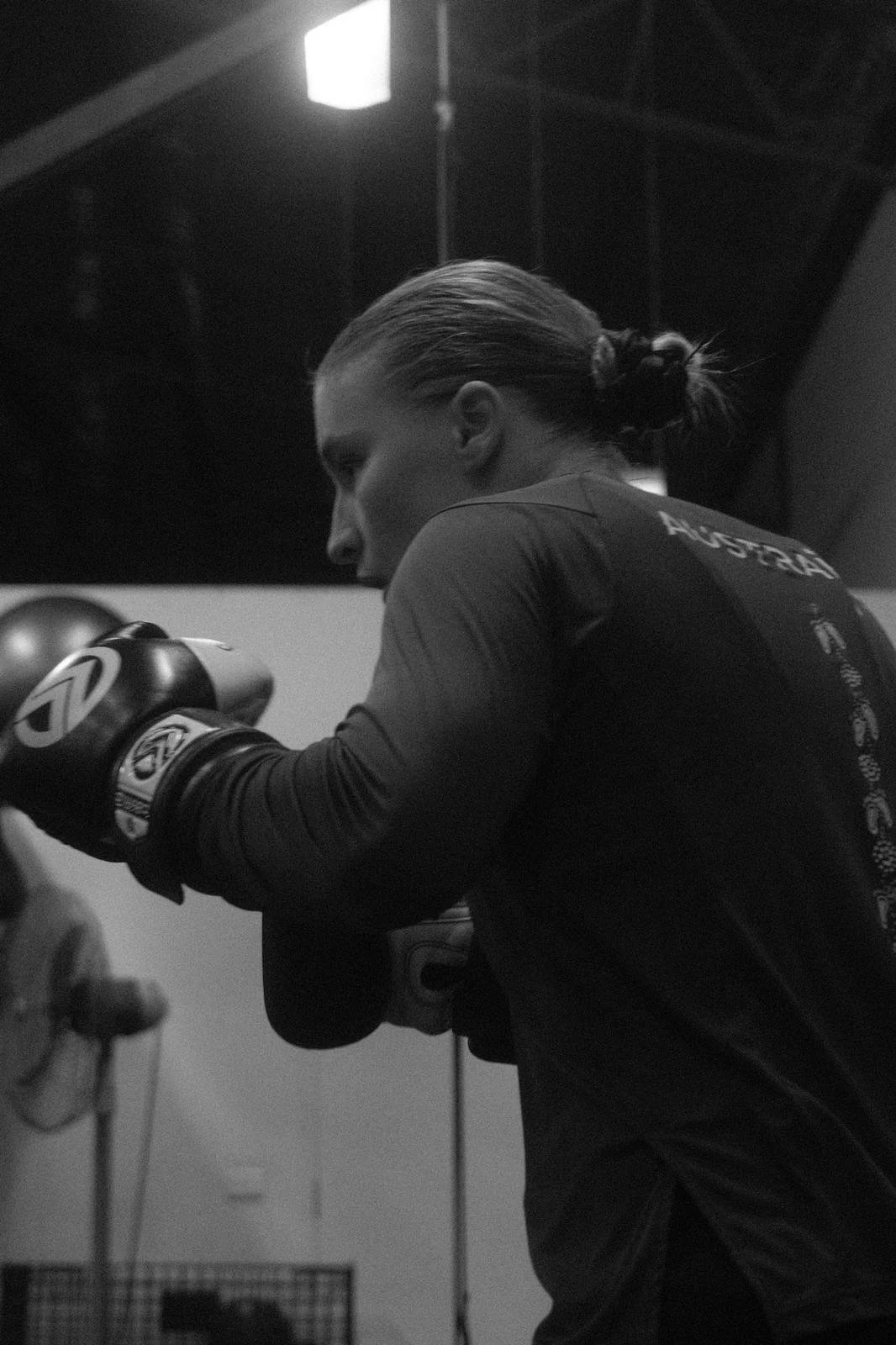A female boxer with tied back hair wearing boxing gloves and training in a gym.