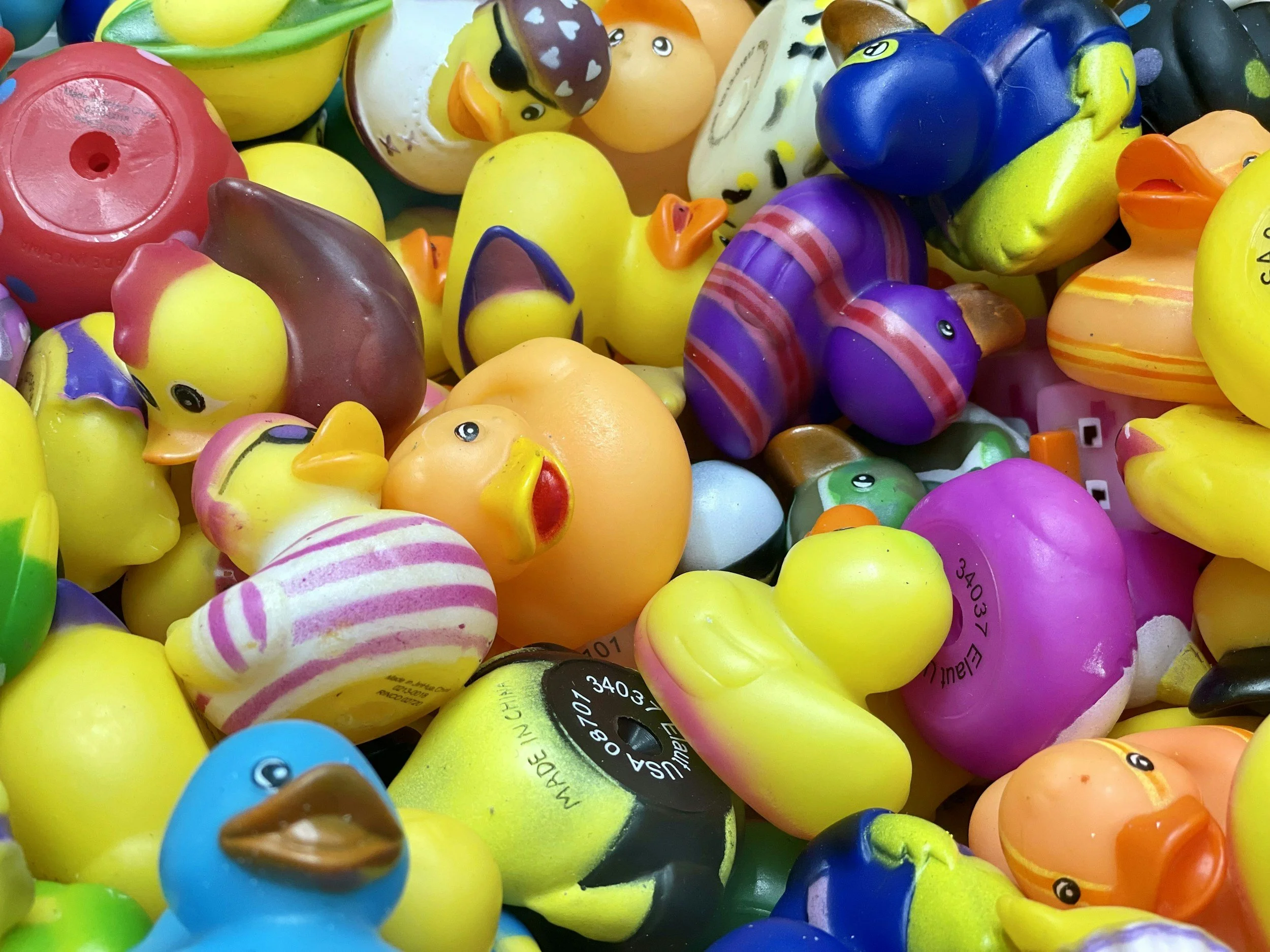 Colorful collection of plastic rubber duck toys with various designs and expressions piled together.