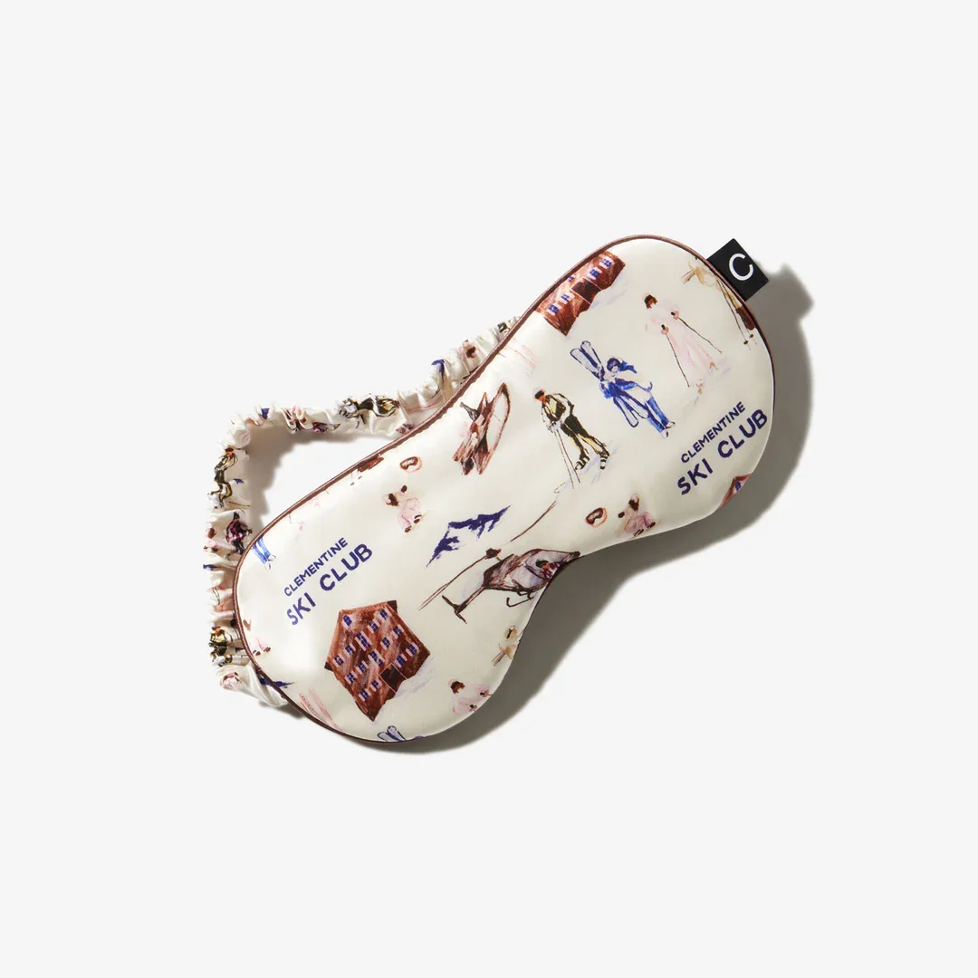 Sleep mask with illustrations of skiers, mountains, and cottages, and the text 'Clementine Ski Club' printed on it.