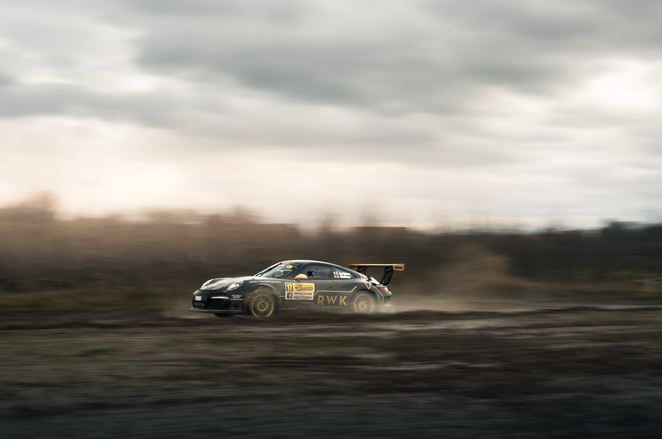 A sleek black race car speeding on a dirt track, with a cloudy sky overhead and motion blur indicating high speed.