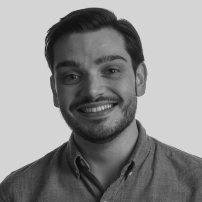 A black and white portrait of a young man with dark hair, a beard, and a smile, wearing a button-up shirt.