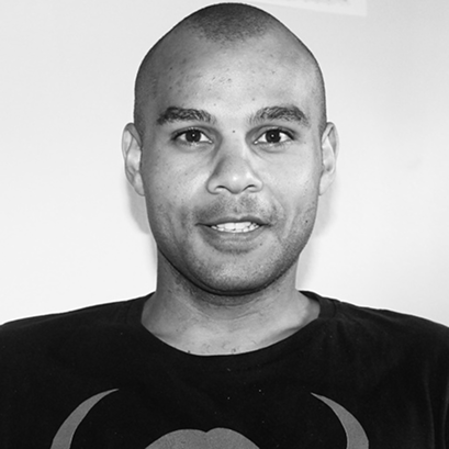 Black and white photo of a smiling man with a shaved head, wearing a dark shirt.