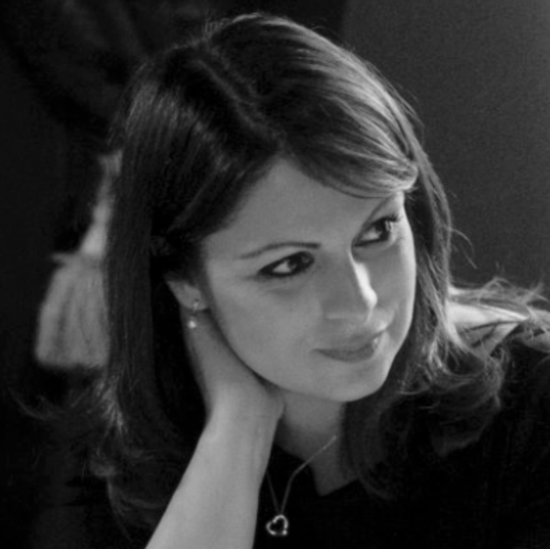 Black and white photograph of a woman with shoulder-length hair, resting her chin on her hand, looking to her right with a slight smile.