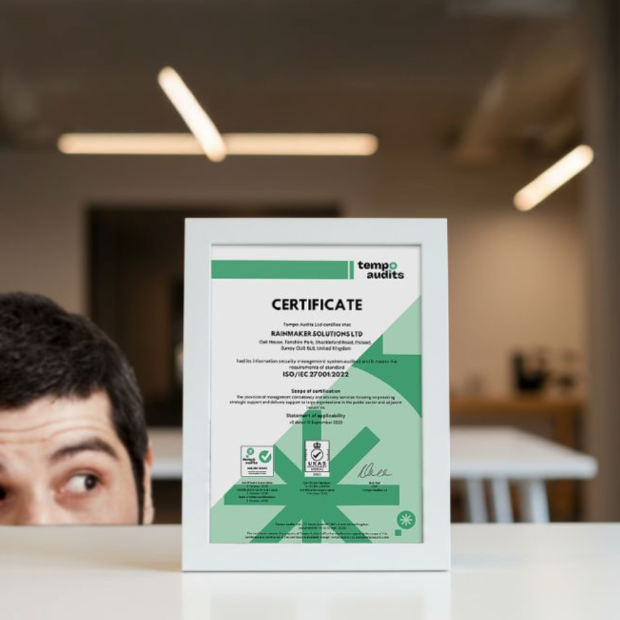 A framed certificate of quality assurance from Tempo Audits awarded to Rainmaker Solutions Ltd, displayed on a white table in an office setting.