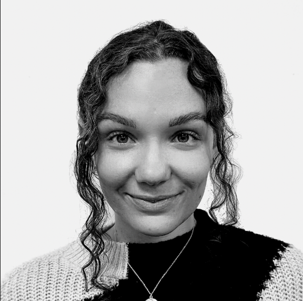 A smiling woman with curly hair wearing a sweater and a necklace.