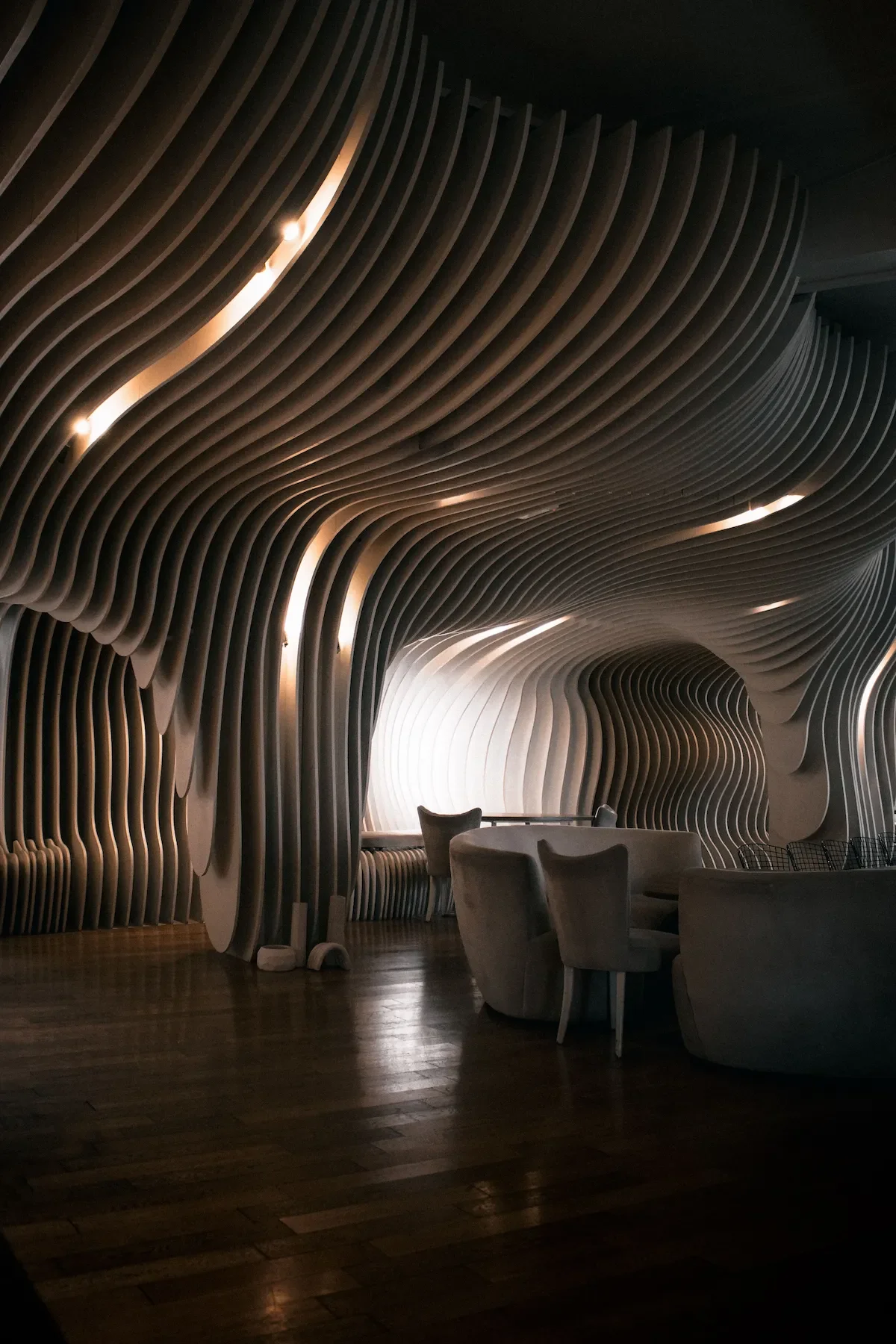 Intérieur moderne avec un plafond design en lattes courbées en bois et un éclairage intégré, comprenant un coin salon avec des fauteuils et une table, ambiance chaleureuse et sophistiquée.