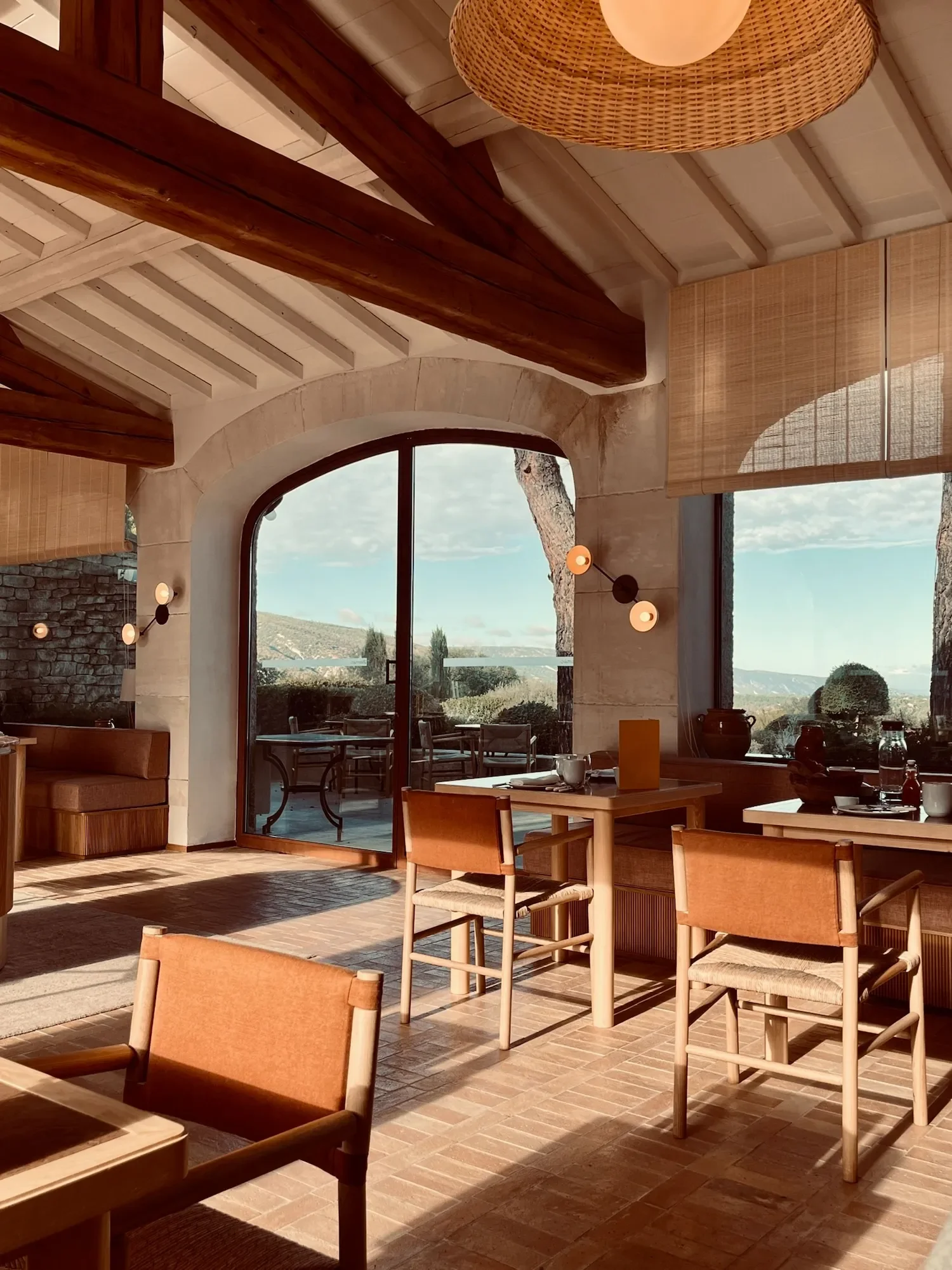Intérieur d'un restaurant avec mobilier en bois, grandes fenêtres avec vue sur la nature, décor moderne avec lumière chaleureuse.