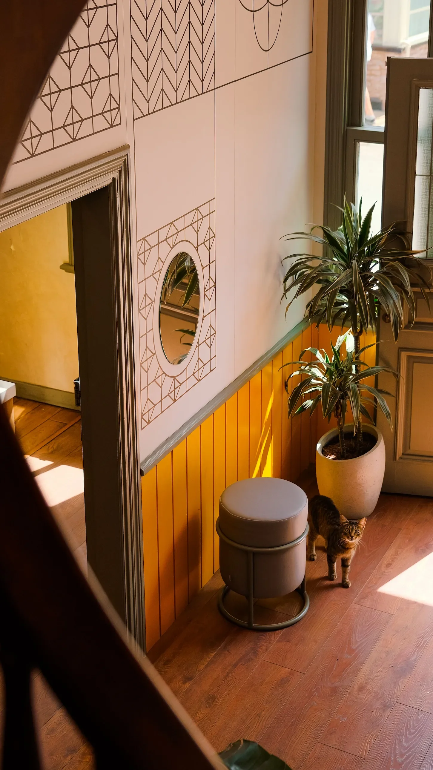 Intérieur d'un hall d'entrée avec un mur décoré de motifs géométriques, des touches de jaune pour dynamiser la pièce. Porte d'entrée ajourée pour laisser entrer la lumière.