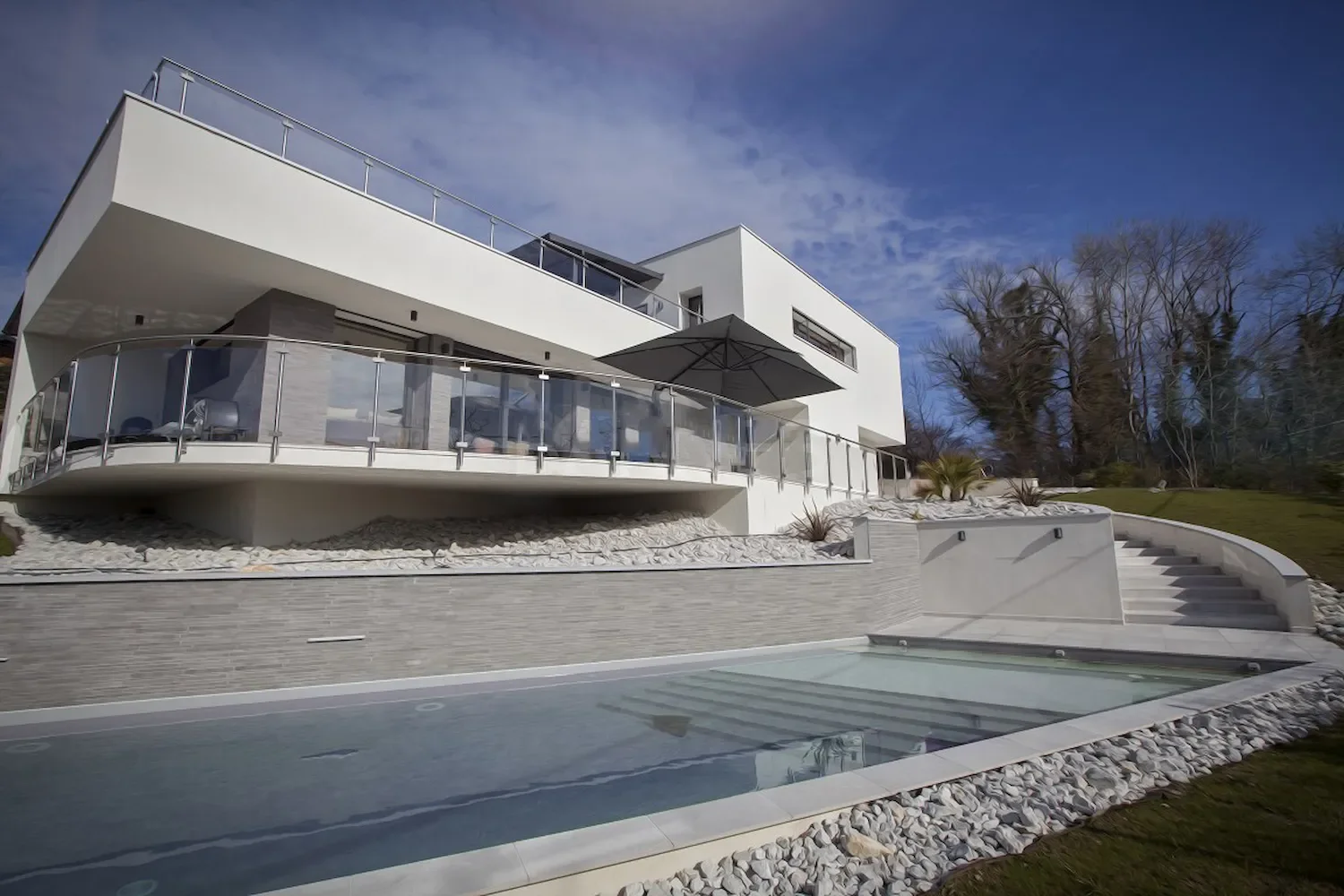 Maison moderne à plusieurs niveaux avec terrasse, vue sur un jardin avec piscine, esprit épuré et minéral.