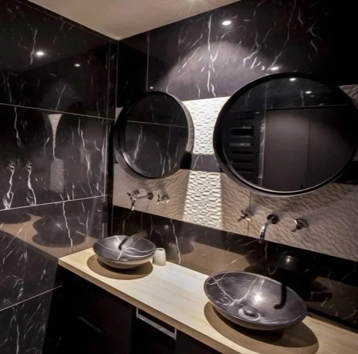 Une salle de bain moderne avec deux vasques en granit noir, un meuble de salle de bain sur mesure ton foncé et bois, deux miroirs ronds et un arrière-plan avec ses rayures blanche (faïences à relief) sur murs noirs (marbre).