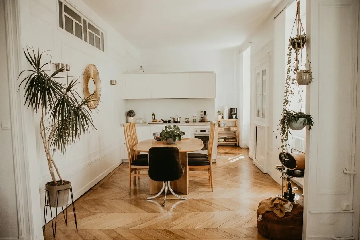 Intérieur d'un appartement de style haussmannien avec une vaste cuisine ouverture sur une lumineuse salle à manger avec un sublime parquet en pointe de Hongrie, plantes en pot suspendus, arrière-cuisine en arrière-plan.