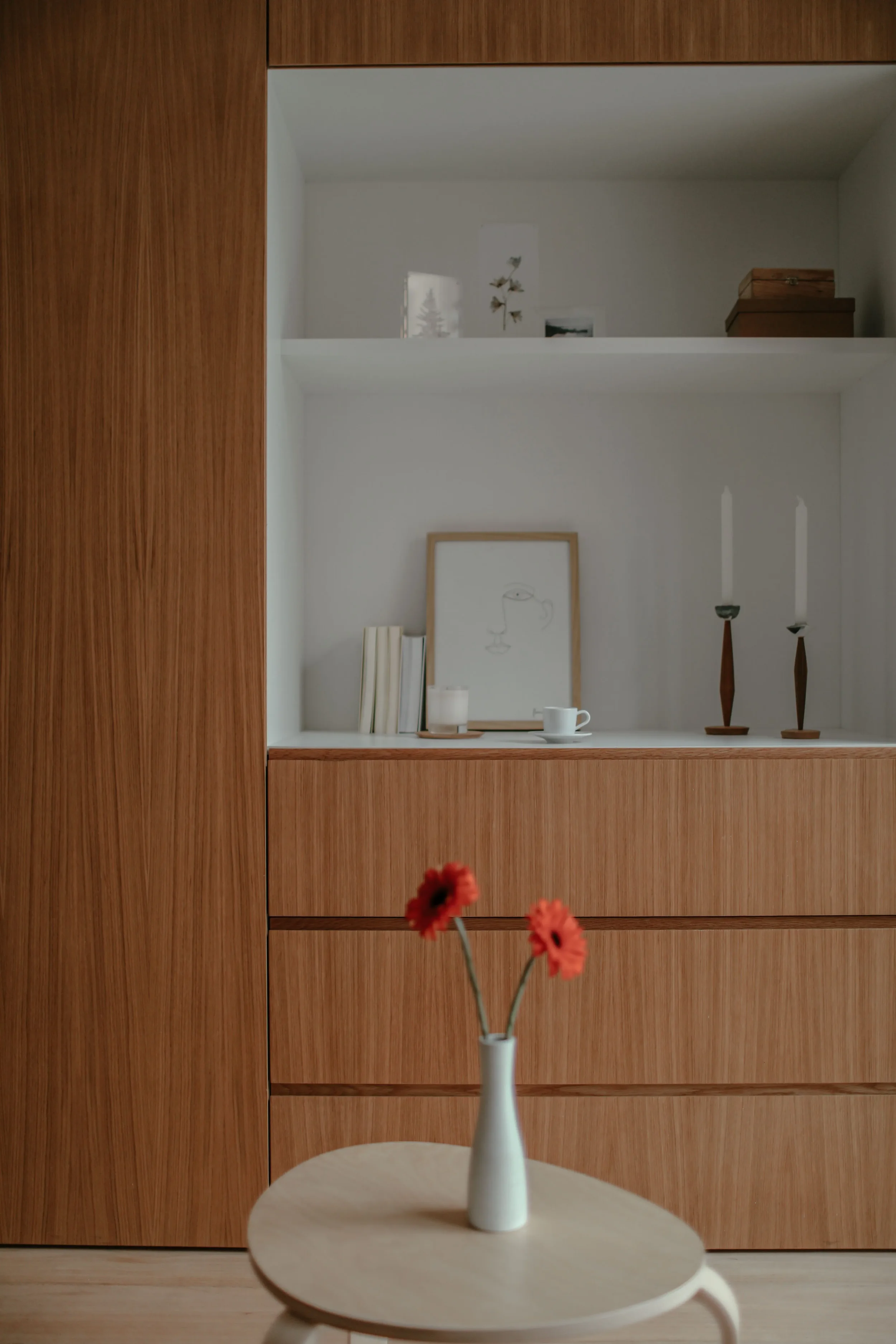 Un séjour avec un agencement sur mesure en bois clair avec rangements et niches décoratives, un mobilier et des objets décoratifs épurés pour un style minimaliste et moderne.