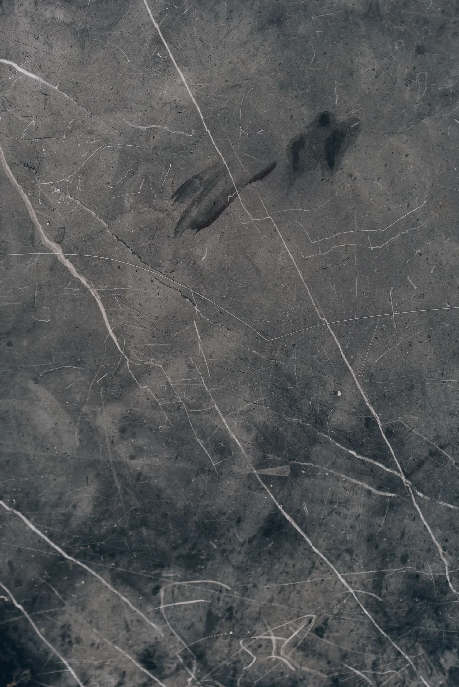 Surface en céramique sombre avec des veines blanches et des marques noires, plusieurs lignes blanches fines traversant la surface.