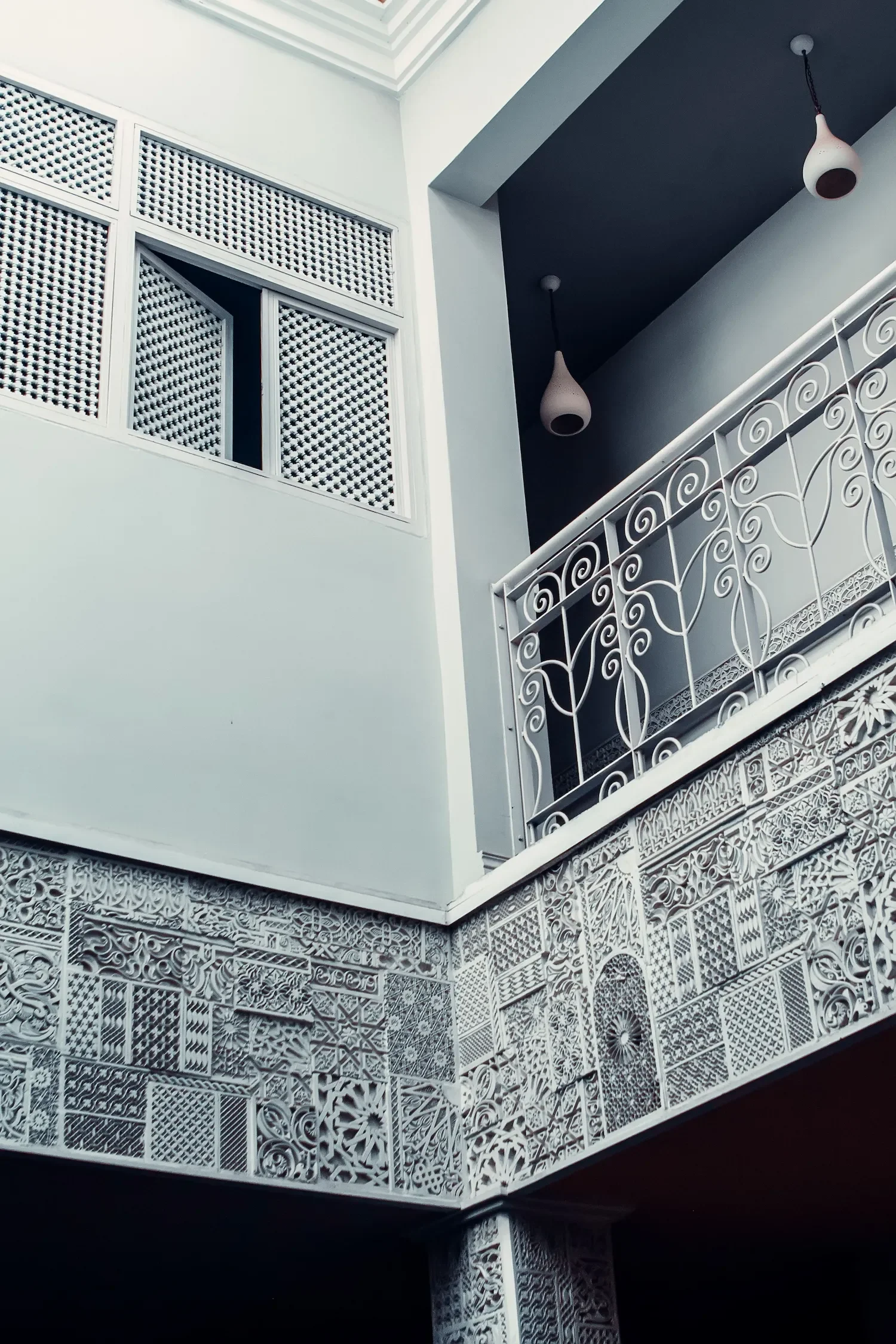 Vue d'une façade intérieure avec des murs en céramique ornés de motifs géométriques, une balustrade en fer forgé et deux suspensions modernes au plafond.