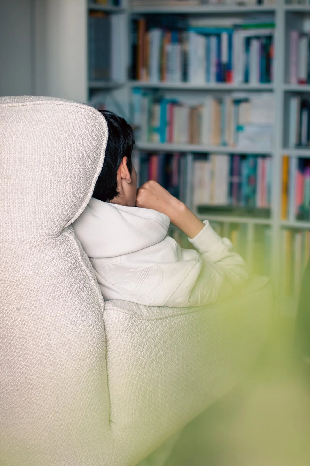 Enfant assis sur un canapé blanc devant une bibliothèque remplie de livres.
