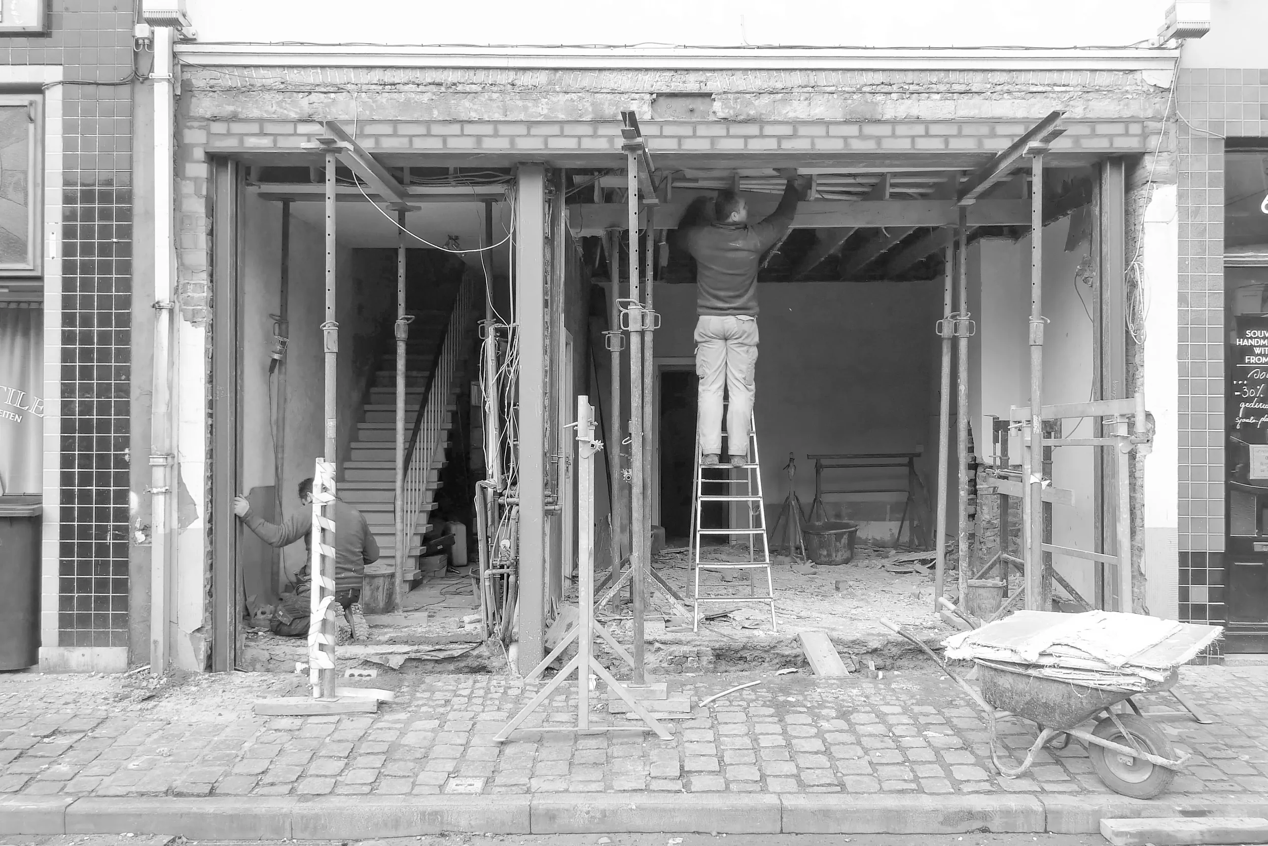 Construction site with a person standing on a ladder working on the building's structure, scaffolding and construction materials in front.