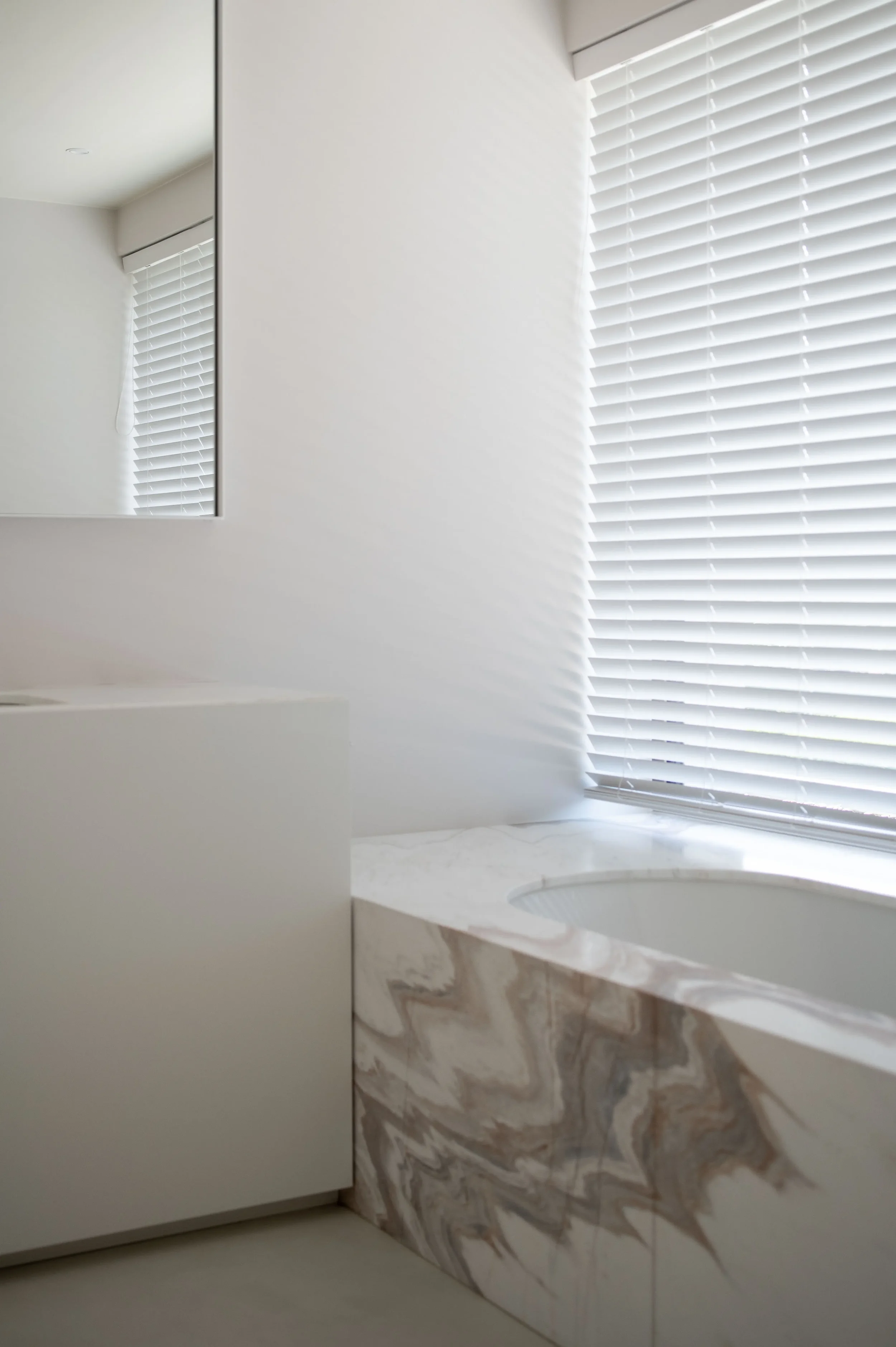 interieur badkamer met bad in onderbouw en badomranding in natuursteen, vloer in mortex