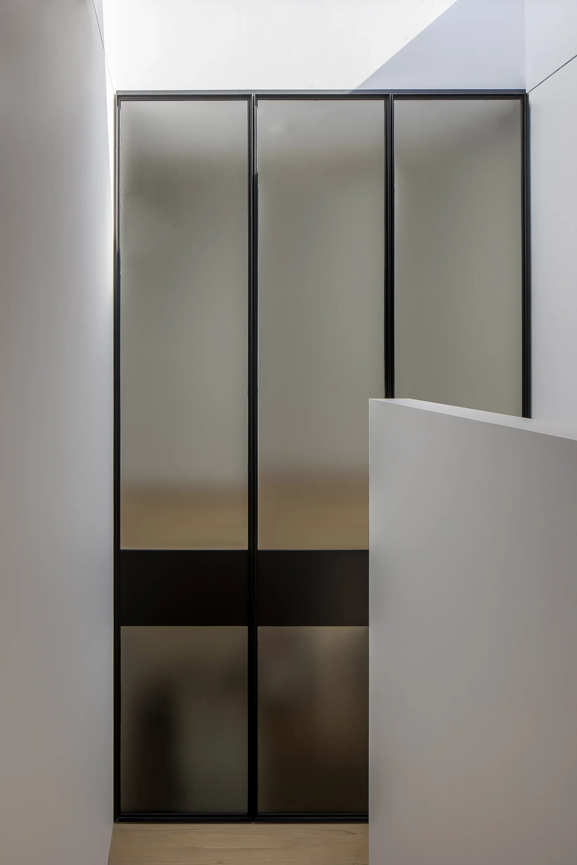 A modern minimalist staircase leading down to a sliding glass door with black frames, white walls, and light wood steps.