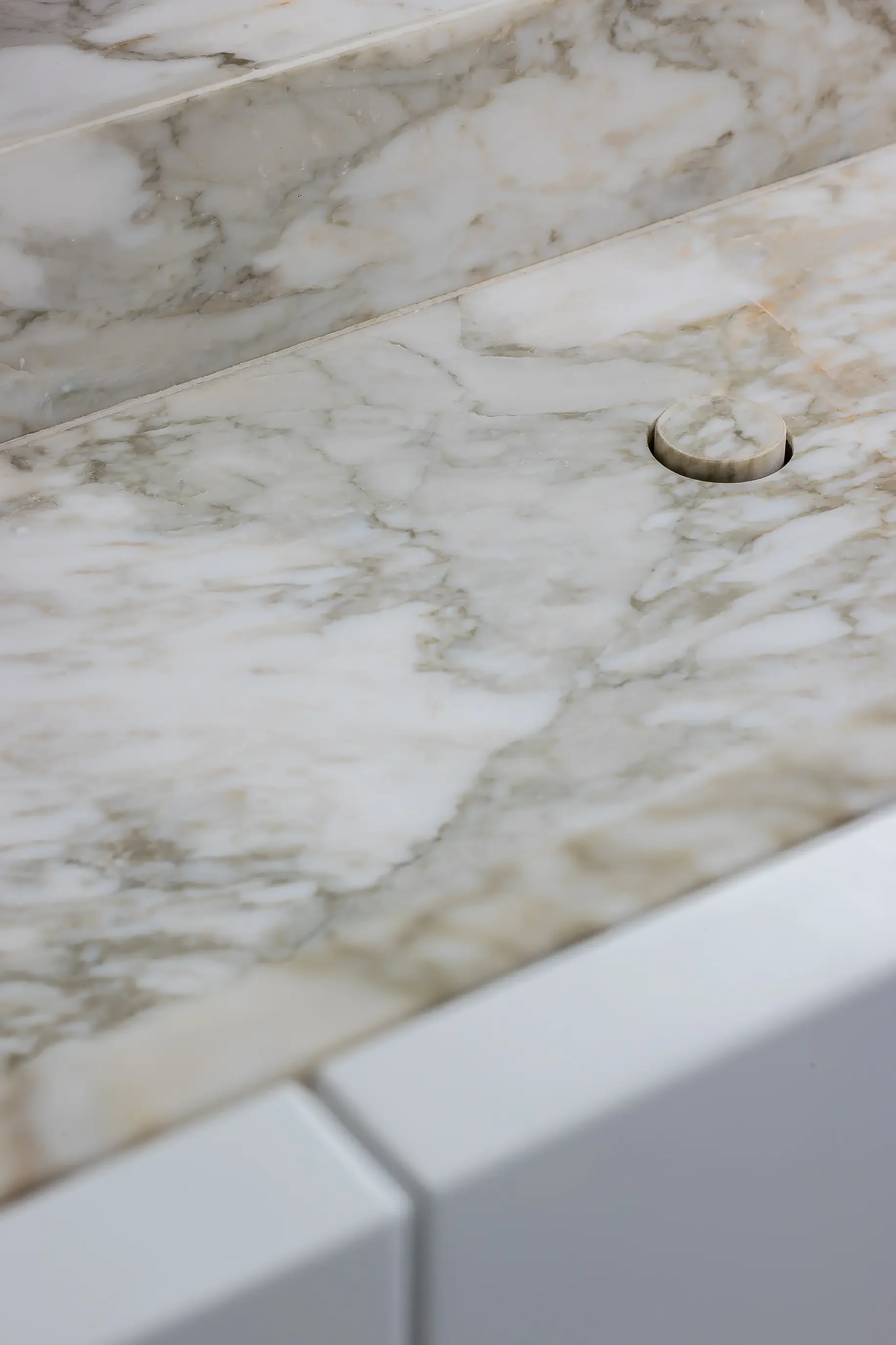 Close-up of a white marble shower with a round marble drain cover.