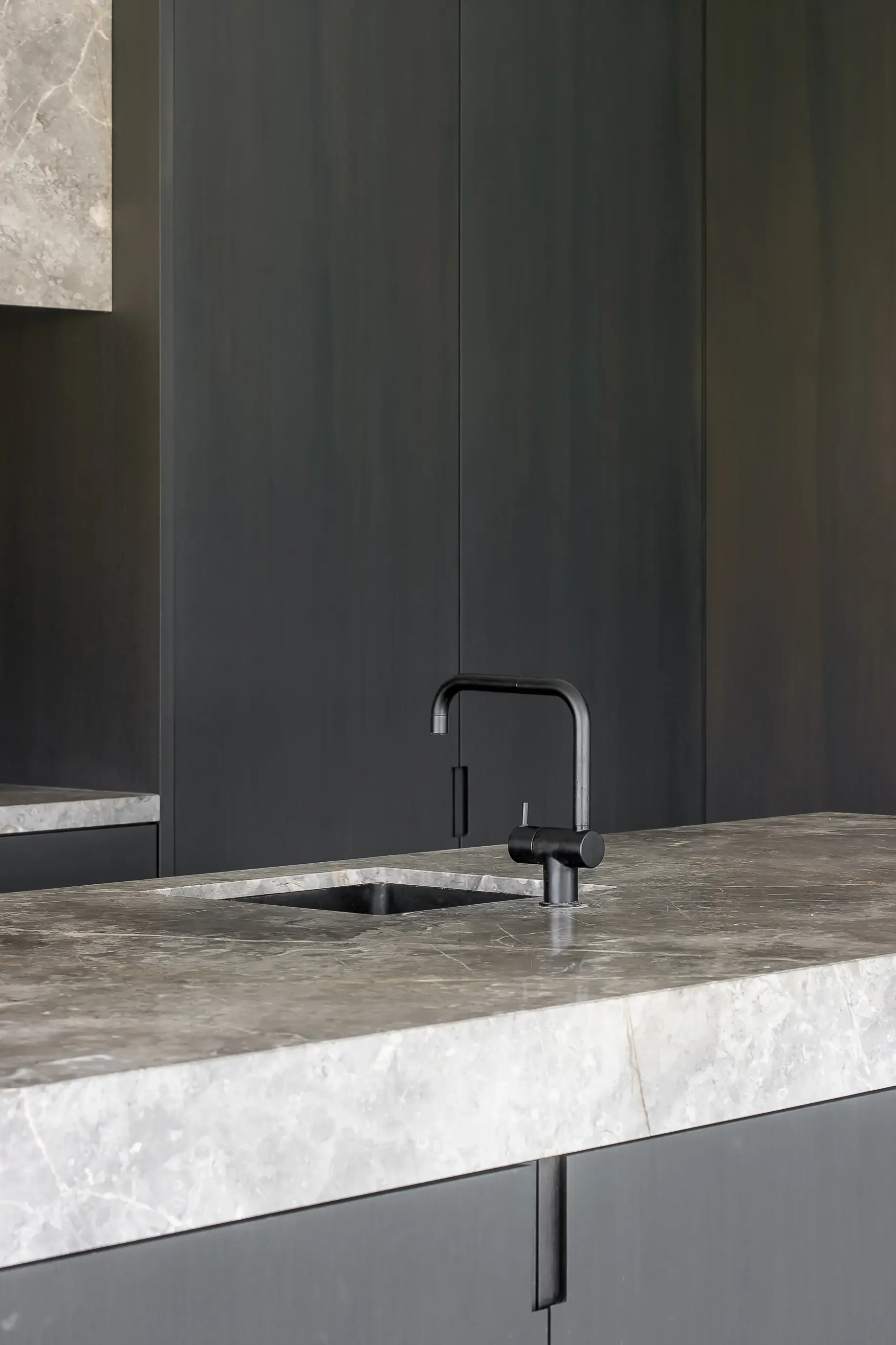Close-up of a modern kitchen countertop with a matte black faucet and a dark gray cabinet in the background.